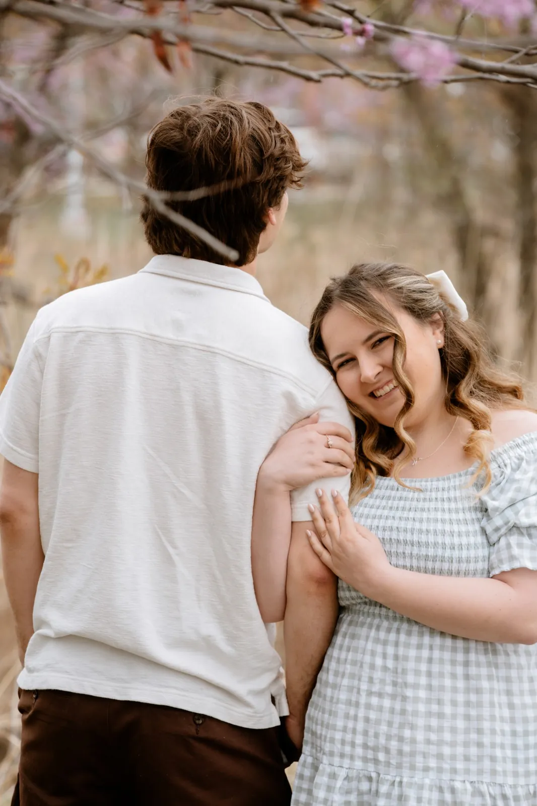 Ally leaning her head on Gavin’s arm and smiling under the redbud branches