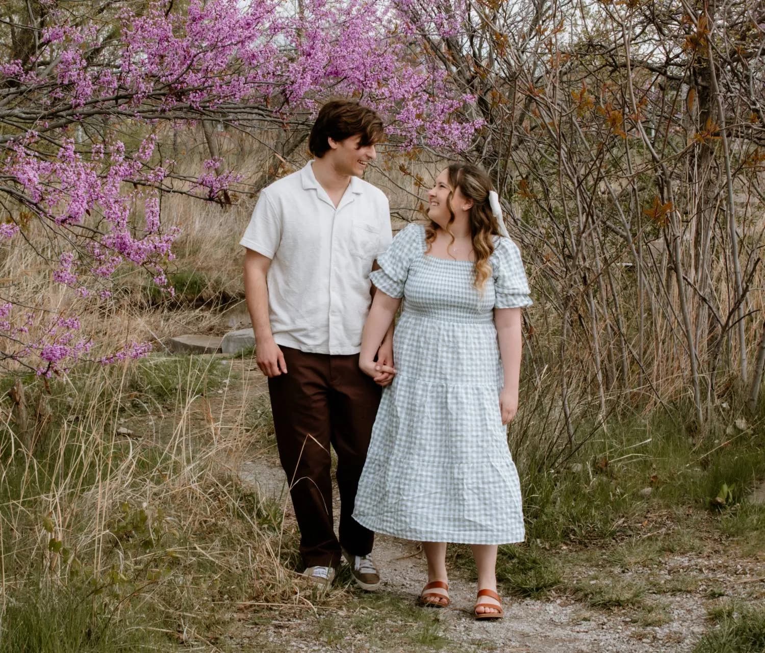 Gavin and Ally walking hand in hand along a path under a pink redbud tree