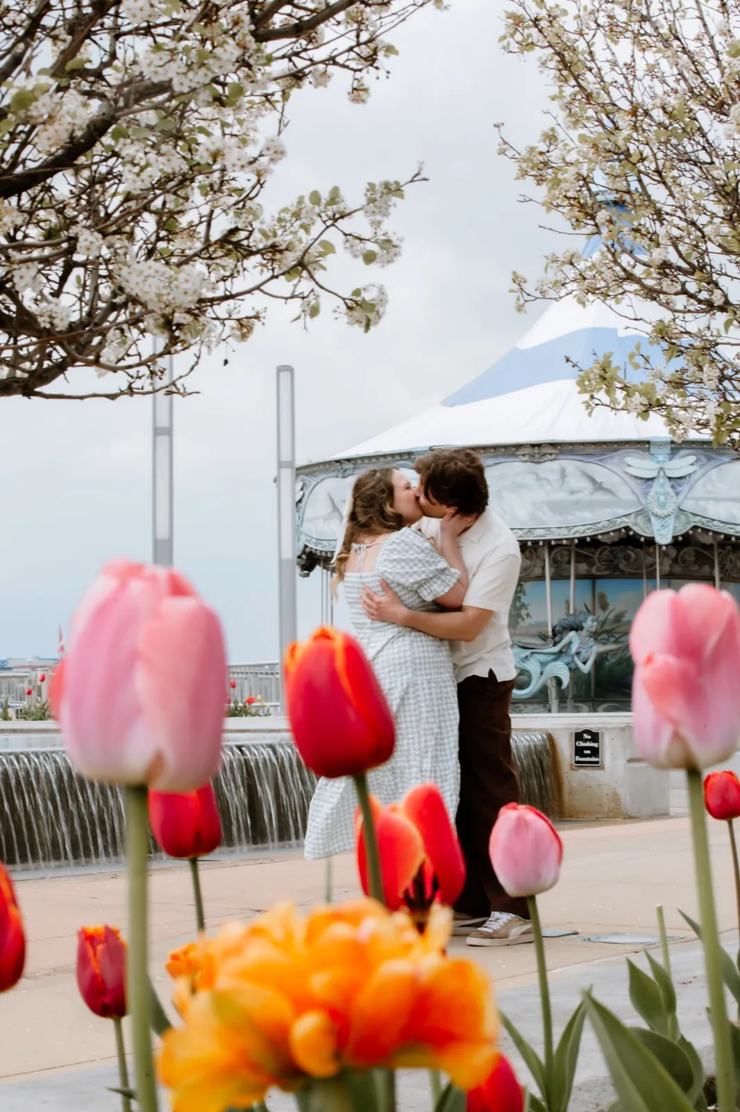 Gavin and Ally kissing beside a carousel, with tulips in the foreground
