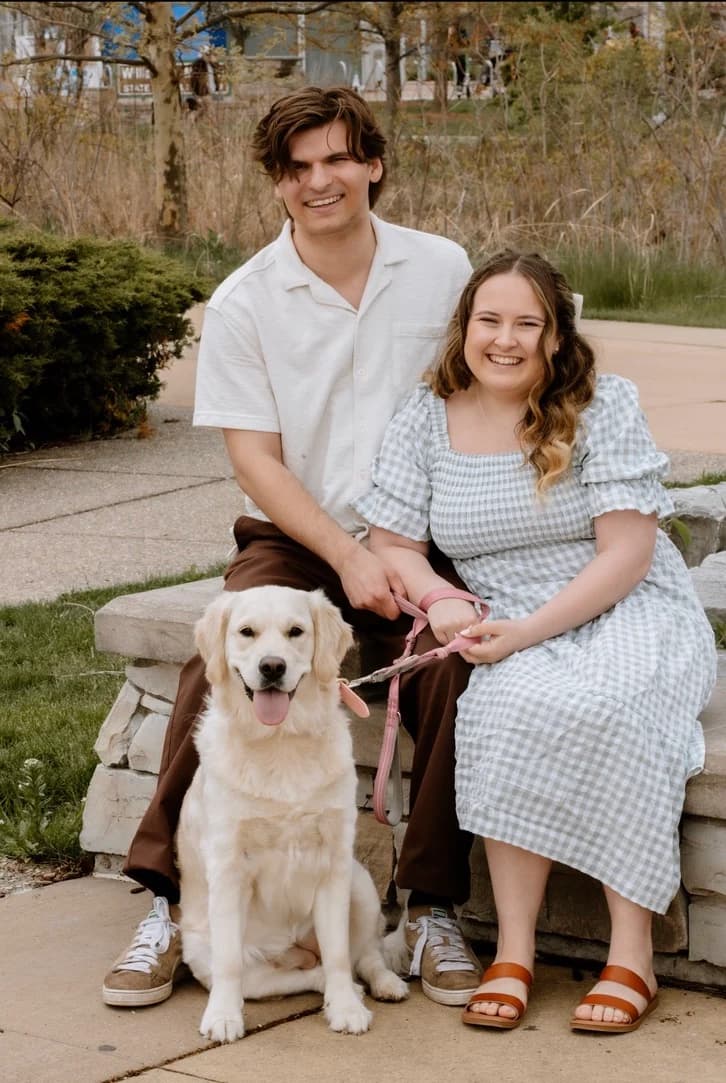 Gavin and Ally sitting on a stone wall with their golden retriever